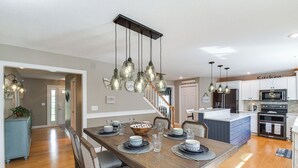 A modern kitchen with white cabinets, a built-in oven, and a dining area with a wooden table set for four. - Rock Island Home w/ Private Yard & Fire Pit Table! (Rock Island)