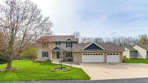 A two-story house with a garage, a well-maintained lawn, and a driveway. - Rock Island Home w/ Private Yard & Fire Pit Table! (Rock Island)