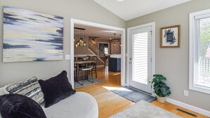 A living room with a sofa, a coffee table, and a painting on the wall. There is a staircase leading to the upper floor. - Rock Island Home w/ Private Yard & Fire Pit Table! (Rock Island)