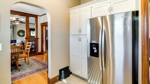 A kitchen with white cabinets, a stainless steel refrigerator, and a dining area with a wooden table and chairs. - Charming Winterset Vacation Rental w/ Yard & Patio (Winterset)