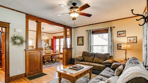 A spacious living room with a ceiling fan, a fireplace, and a dining area with wooden furniture. - Charming Winterset Vacation Rental w/ Yard & Patio (Winterset)