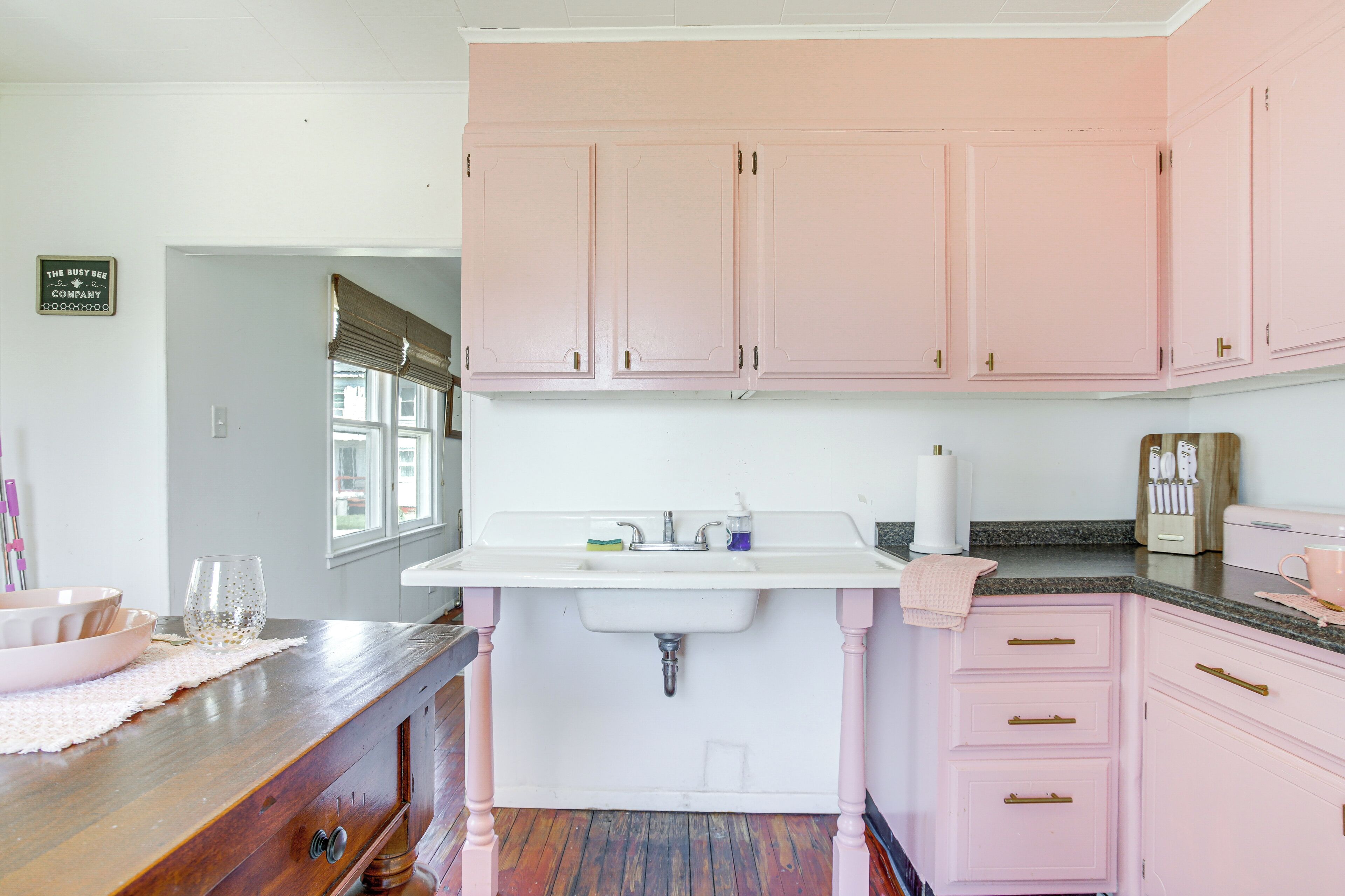 A kitchen with pink cabinets, a white sink, and a wooden countertop.