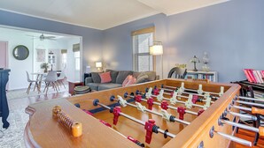 A spacious living room with a foosball table, a sofa, and a dining area with chairs and a table. - Pet-friendly Smith Island Cottage w/ Golf Cart! (Smith Island)