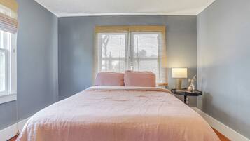 Une chambre à coucher avec un grand lit, une table de chevet avec une lampe et une fenêtre avec des stores.
