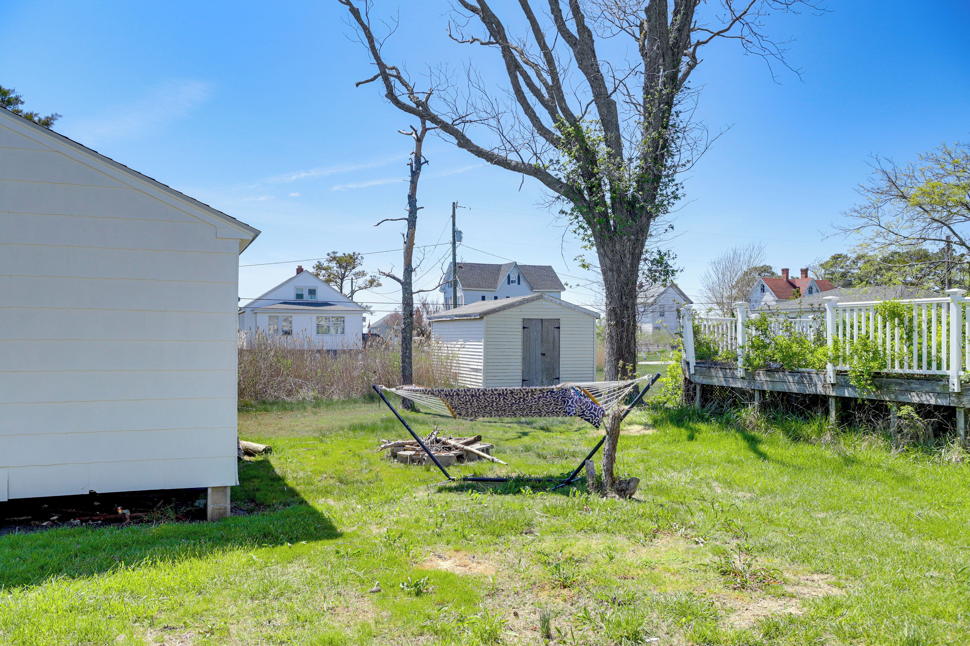 Ein grünes Rasenstück mit einer Hängematte, einem kleinen Schuppen und einem weißen Haus.