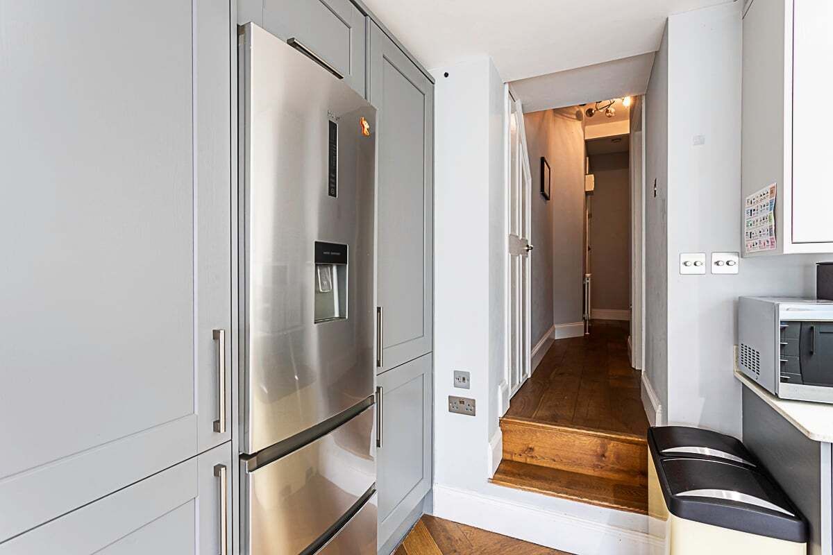 A modern kitchen with stainless steel appliances, a wooden floor, and a white interior.