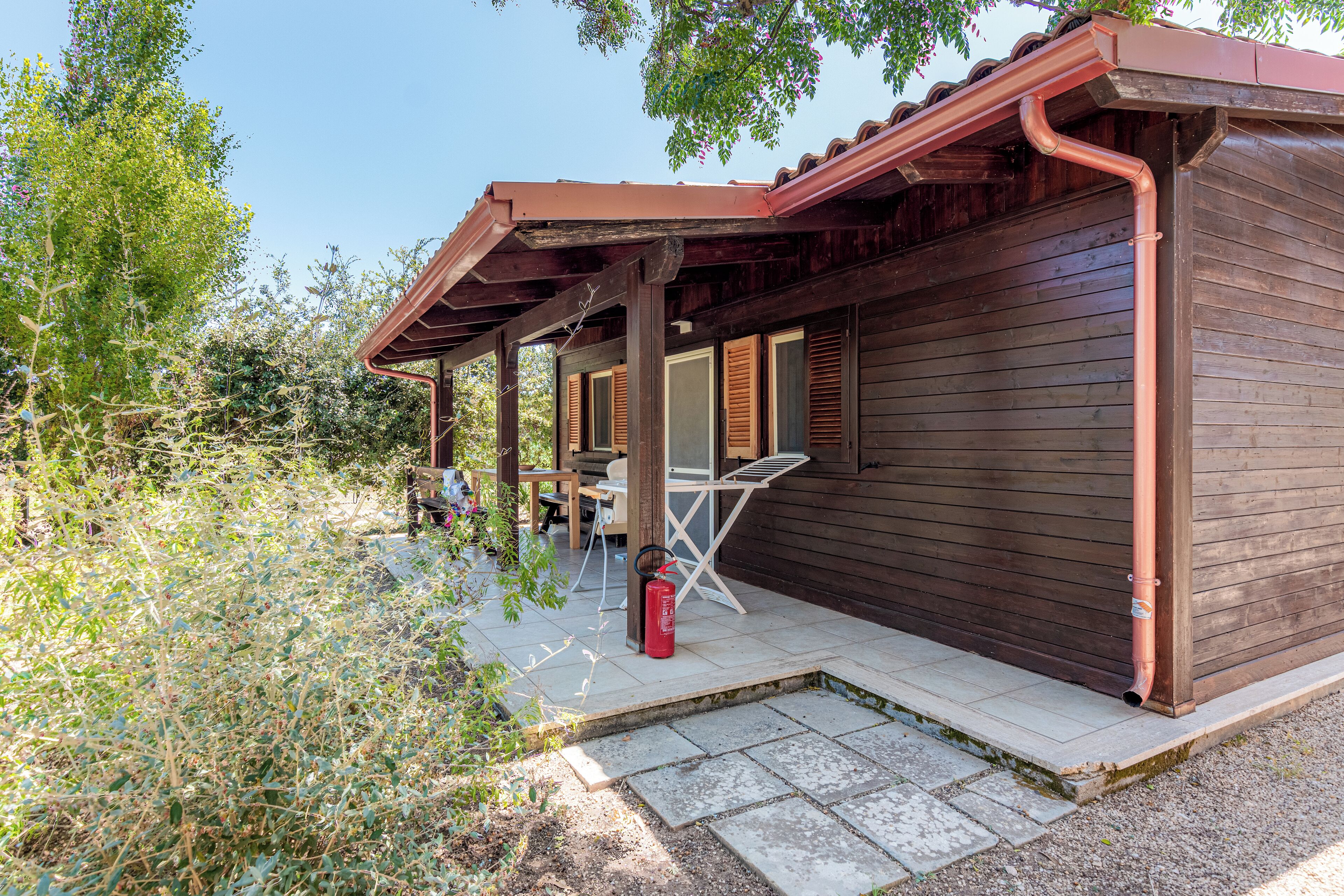 A wooden cabin with a covered patio, a fire extinguisher, and a table and chairs.