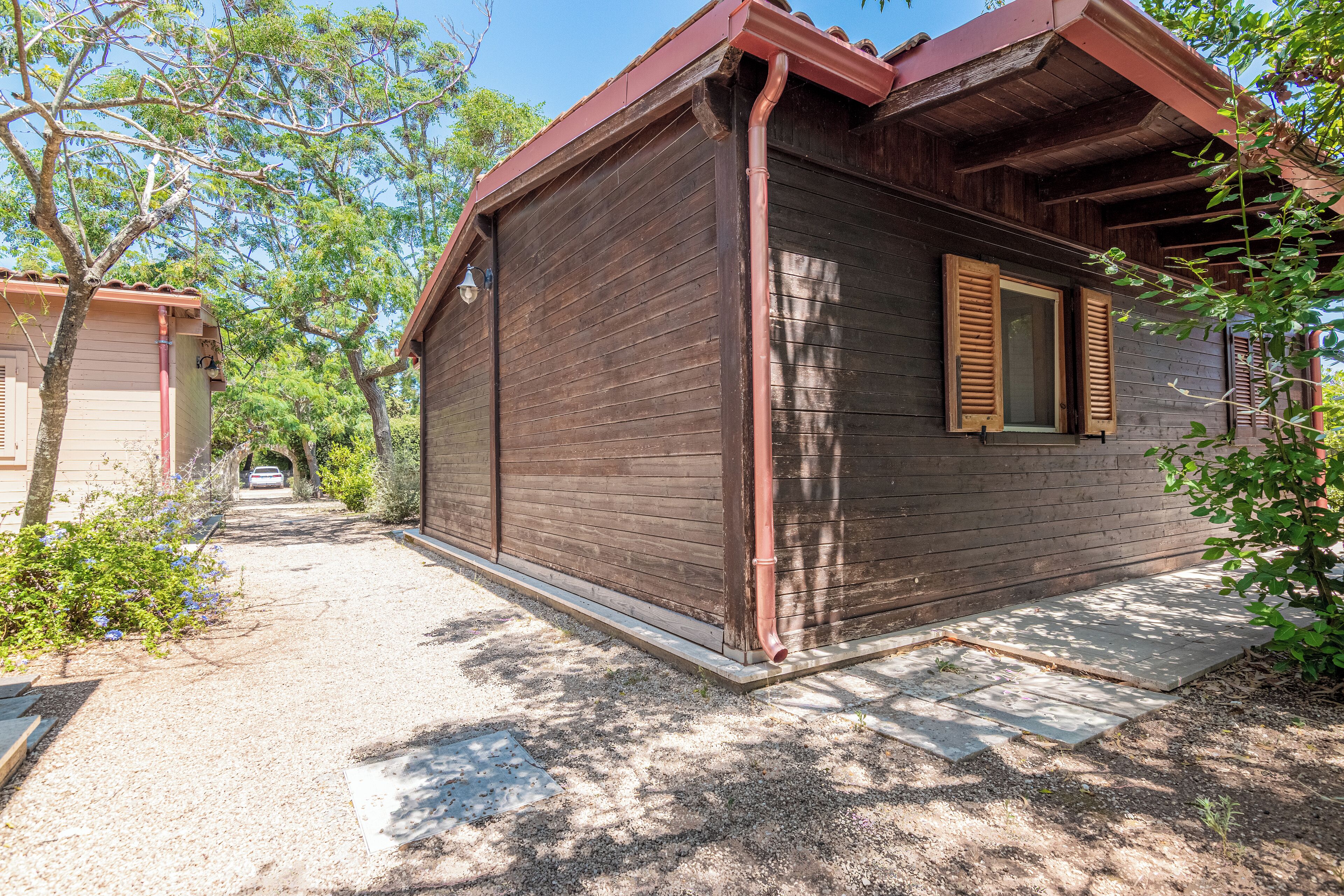 A wooden building with a red roof, a window with wooden shutters, and a gravel driveway.