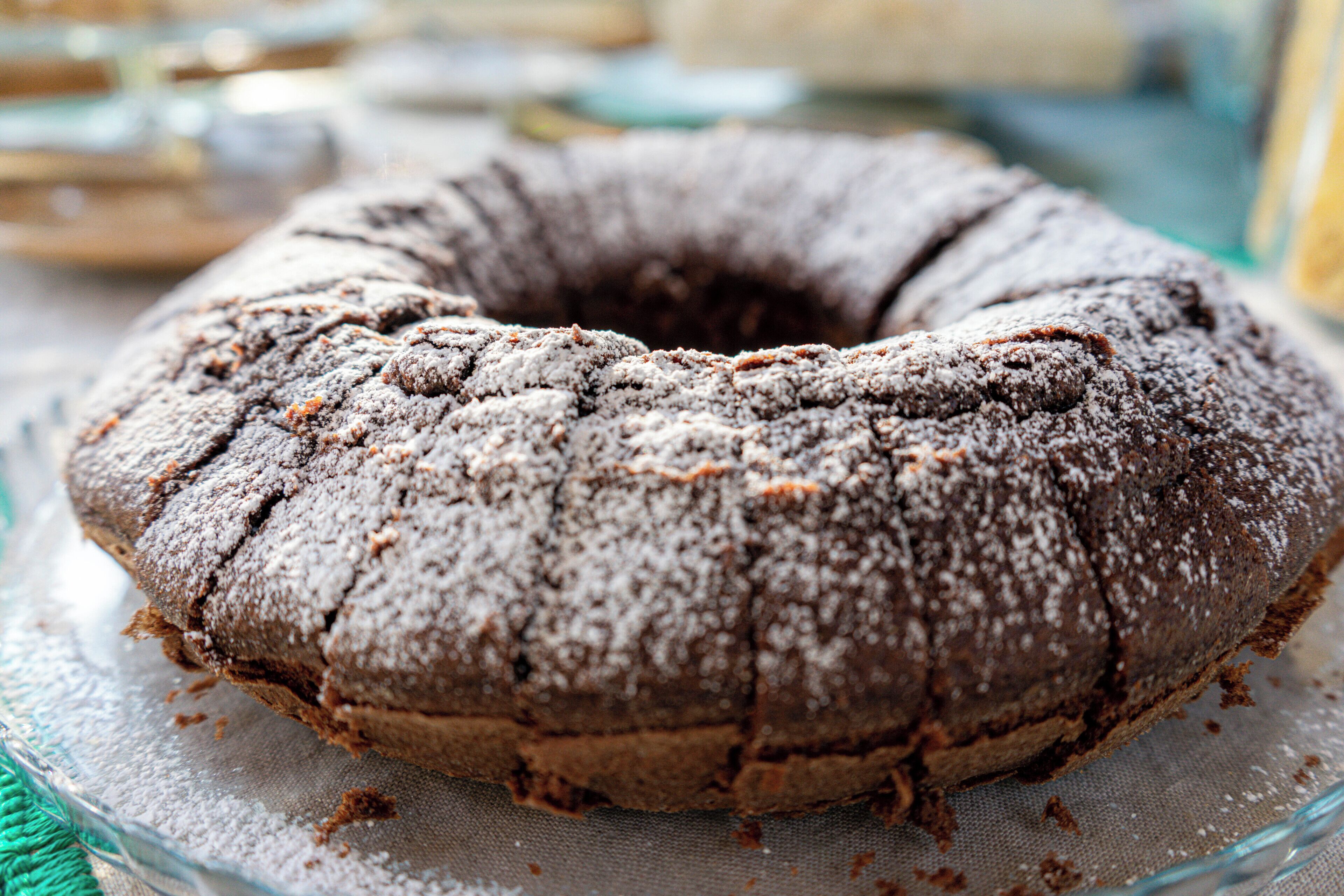 Un gâteau au chocolat en forme de couronne, présenté sur une assiette en verre, avec un tissu placé en dessous.