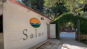 A building with the name 'Salos' on its exterior wall, a circular mural, and a gravel pathway leading to a gated entrance. - BIO AGRITURISMO SALOS (Otranto)