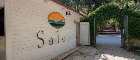 A building with the name 'Salos' on its exterior wall, a circular mural, and a gravel pathway leading to a gated entrance.