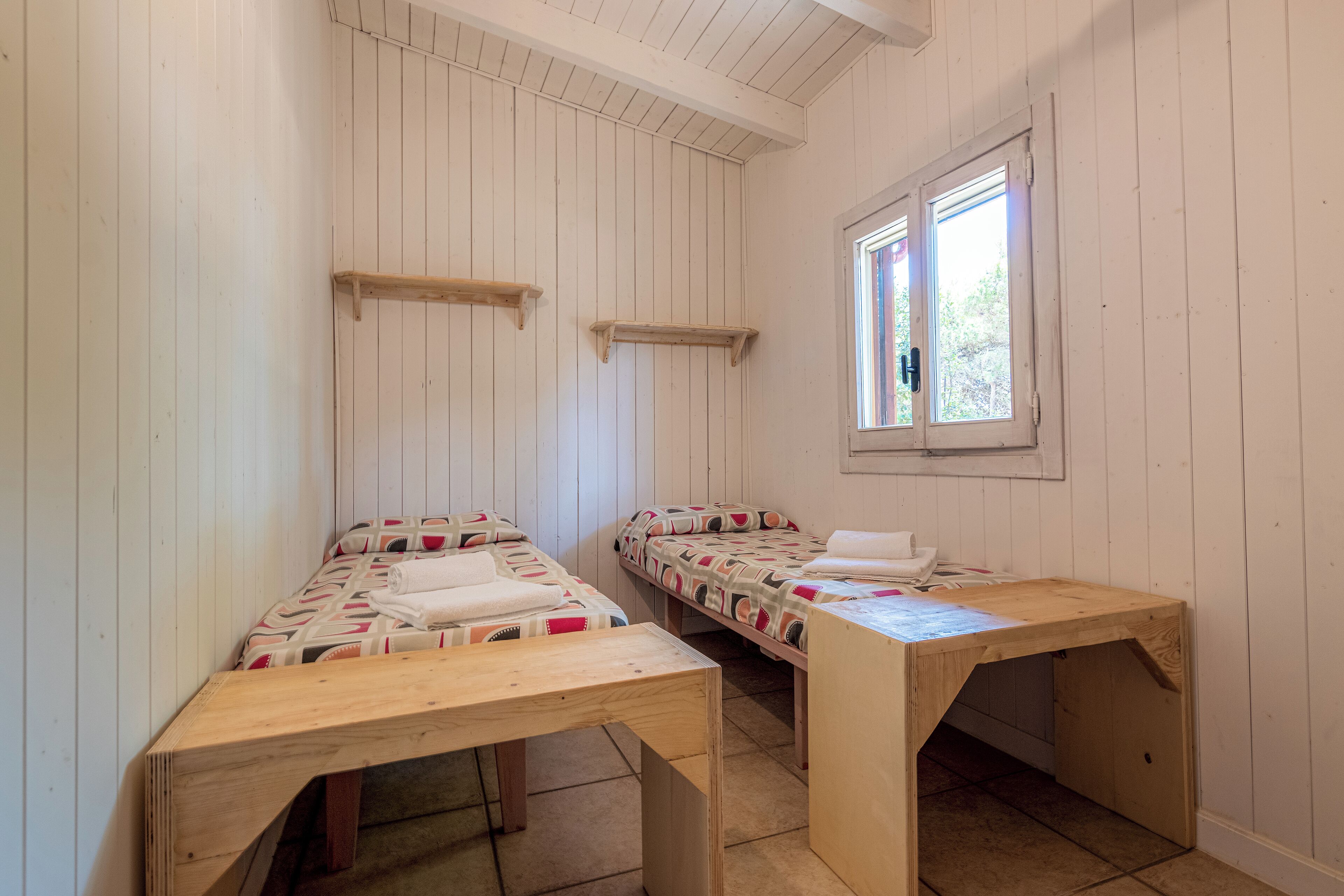 A room with two wooden beds, a window, and a wooden desk.