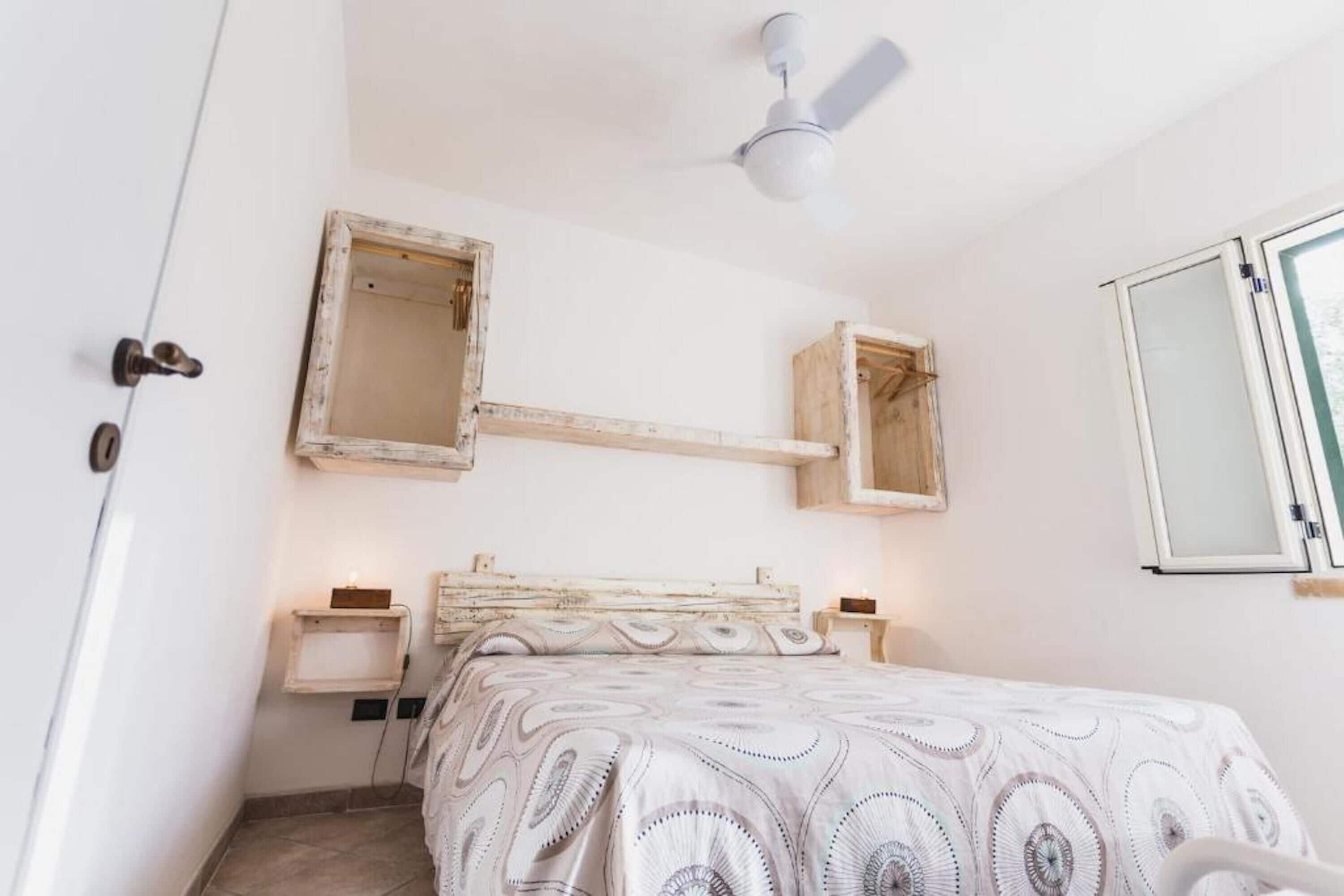 A bedroom with a bed, a ceiling fan, a window, and a door.