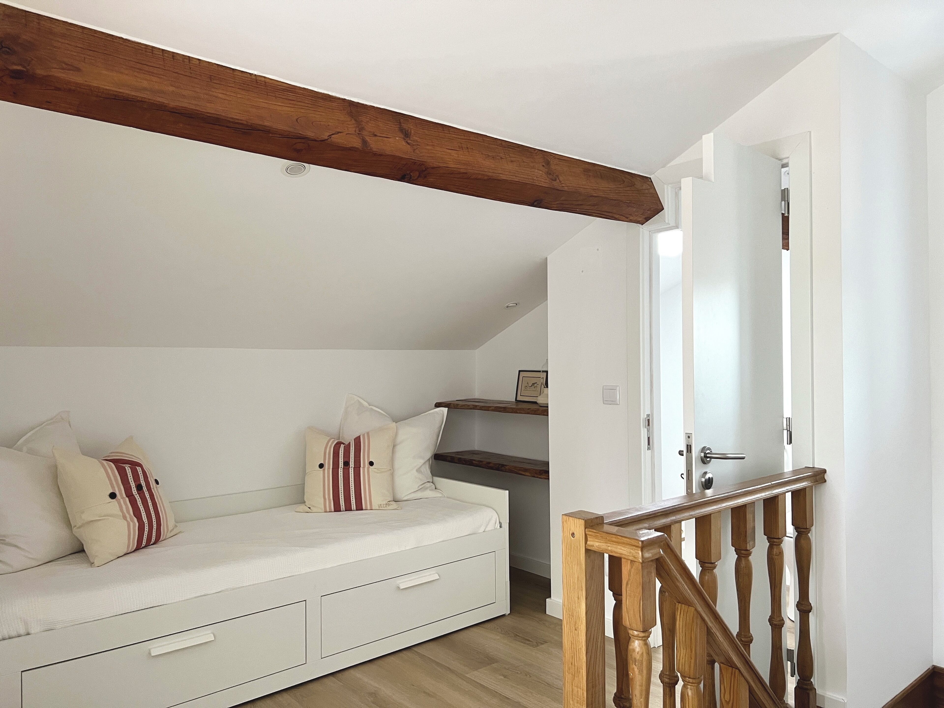 A cozy room with a white sofa, wooden beams, a wooden staircase, and a white door.