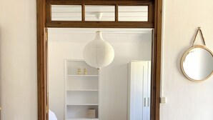 Ein Schlafzimmer mit Holztürrahmen, einem Bett, einer Pendelleuchte, einem Spiegel und einem weißen Kleiderschrank.