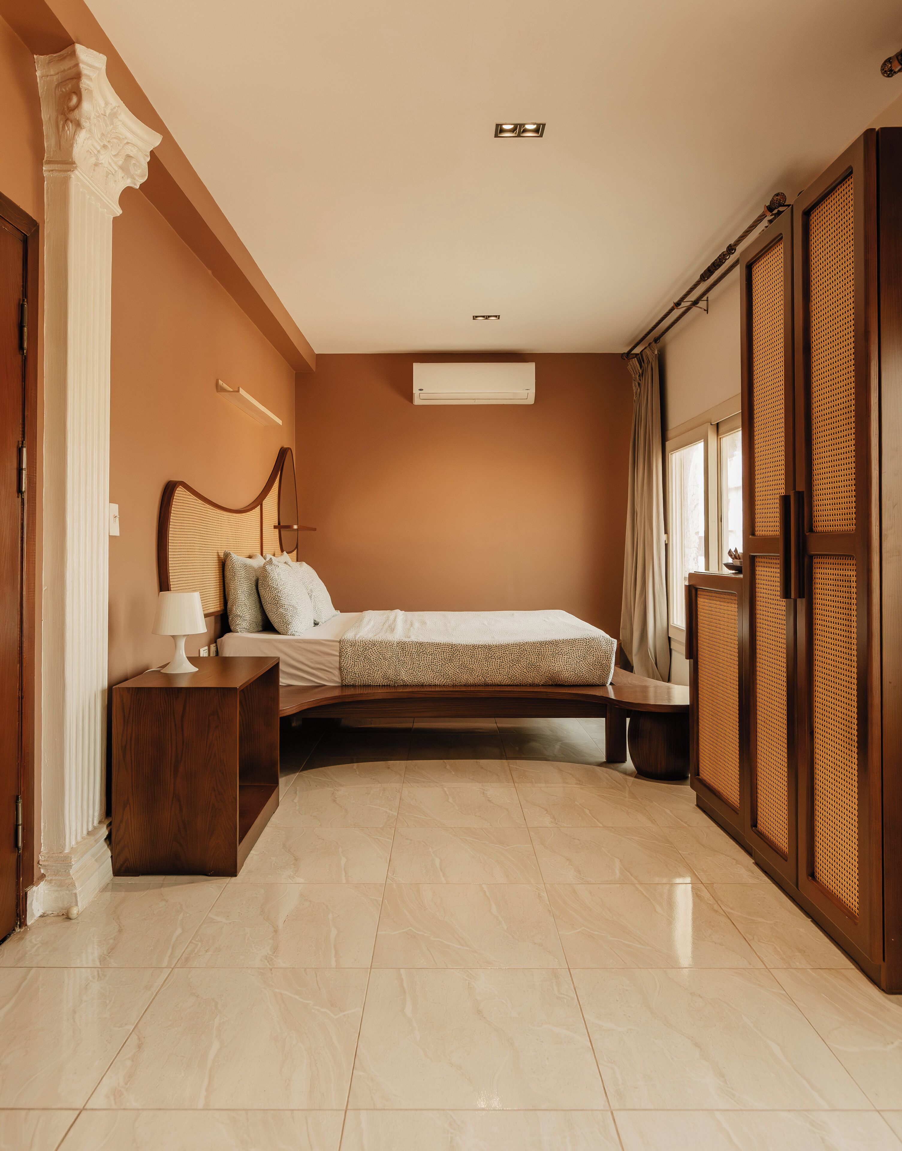 A bedroom with a bed, bedside table, lamp, air conditioning unit, and a wardrobe.