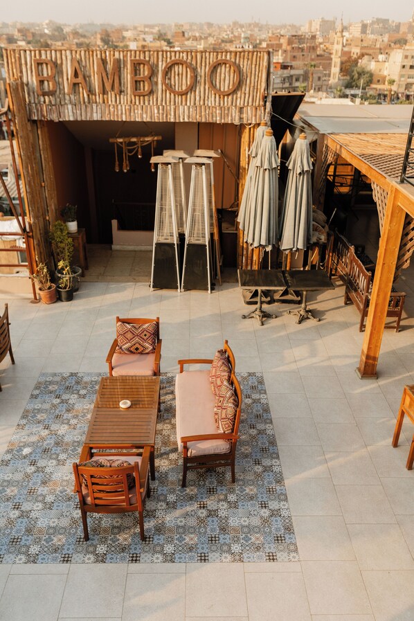 A rooftop patio with a bamboo-themed entrance, outdoor seating, and umbrellas. - Jimmy Pyramids Hotel (Giza)