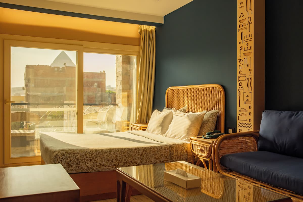 A hotel room with a bed, a sofa, a table, and a view of a building through a window.