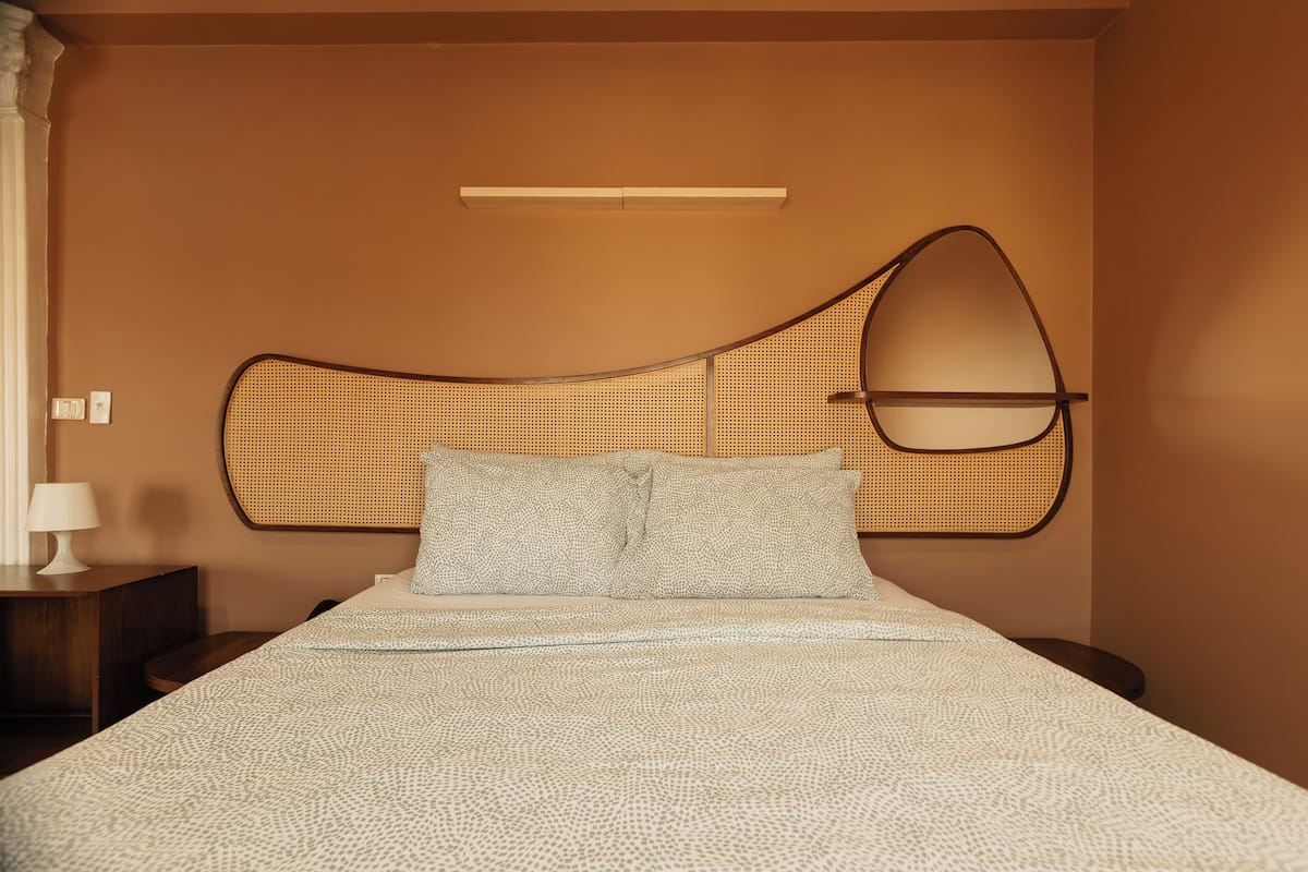 A bed with a woven headboard, a bedside table with a lamp, and a wall-mounted light fixture.