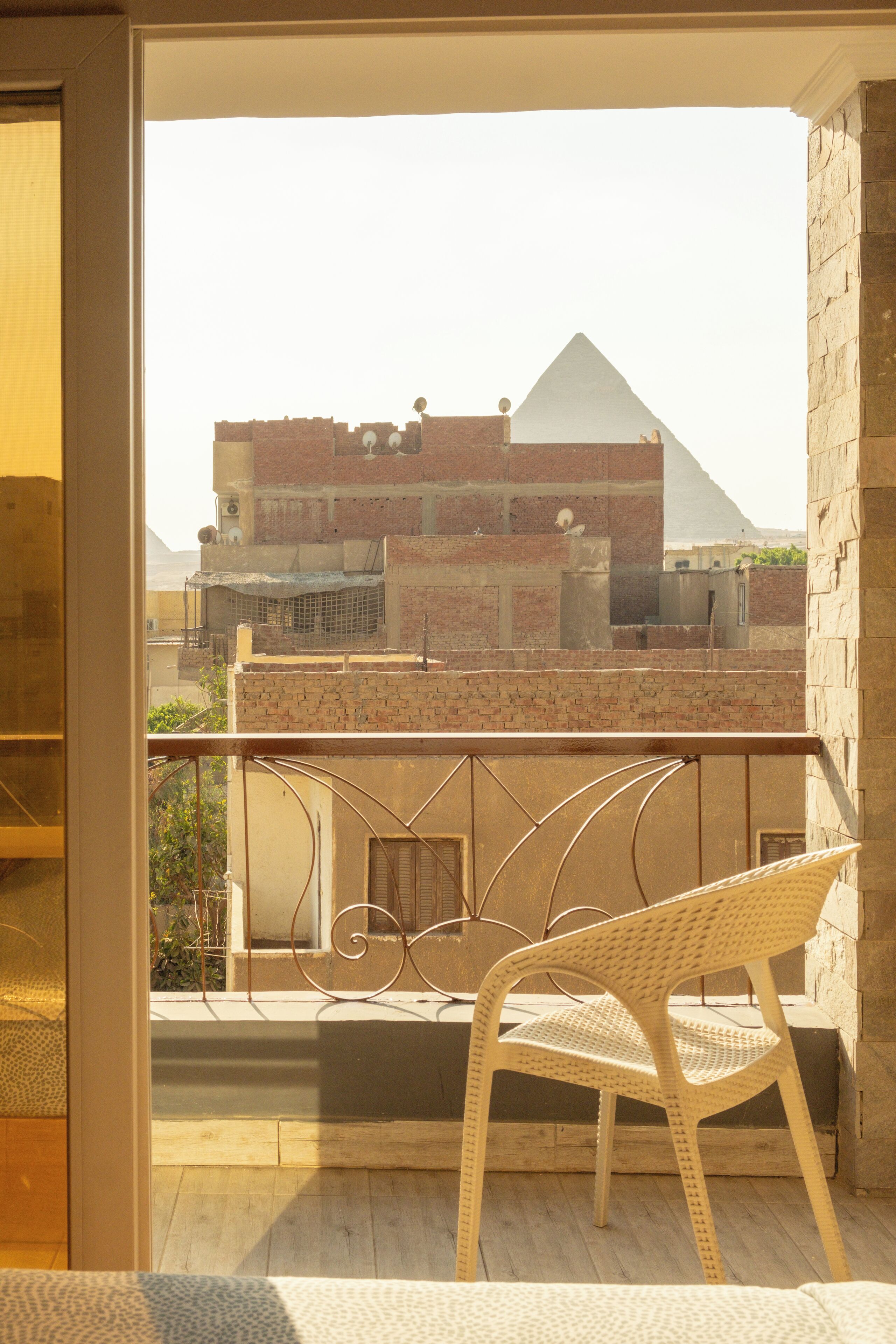 A balcony with a wicker chair, a view of a pyramid, and a building with a flat roof.