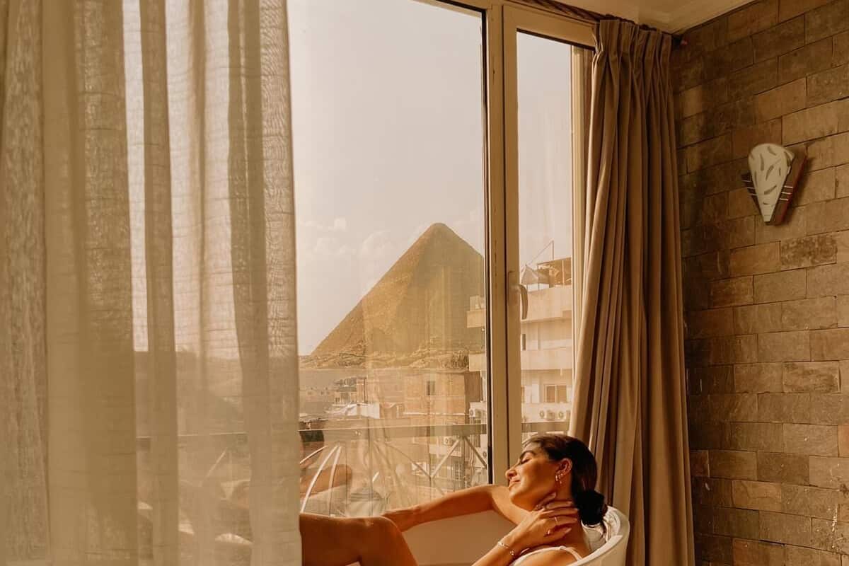 A room with a bathtub, a large window, and a view of a mountain.