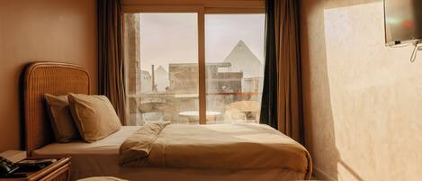 A hotel room with two beds, a television, a window with curtains, and a view of buildings.