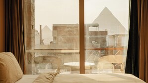 A hotel room with a bed, a window with curtains, and a view of a pyramid. - Jimmy Pyramids Hotel  (Giza)