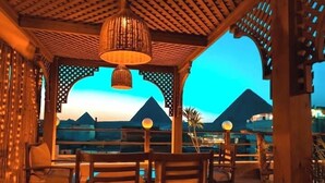 A terrace with wooden furniture and a view of pyramids at dusk. - Jimmy Pyramids Hotel  (Giza)