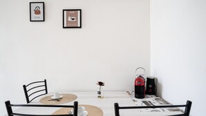 A minimalist dining area with a table set for two, framed pictures on the wall, and a coffee machine. - Bari Cozy Apartment by Wonderful Italy (Bari)
