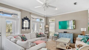 A living room with a white sofa, a coffee table, wicker chairs, a TV, and a ceiling fan. - 5BR Luxury Home with Multiple Lounges + Private Pool | La Contenta (Destin)