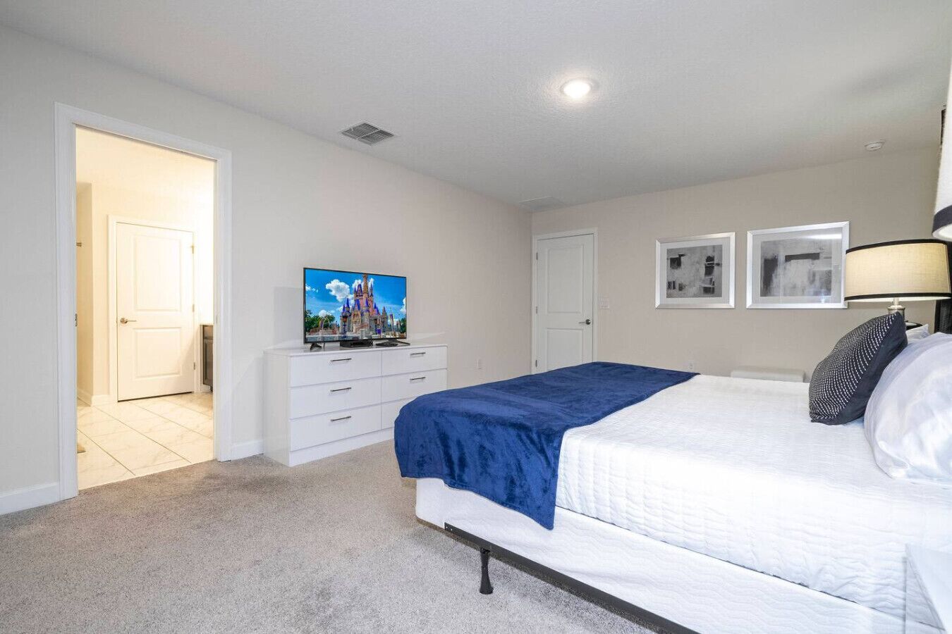 A bedroom with a bed, a dresser, a television, and a door leading to another room.