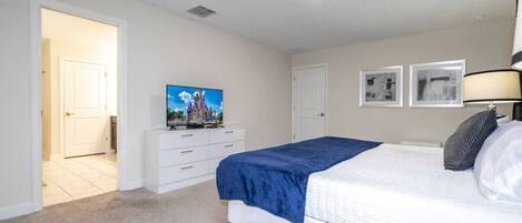 A bedroom with a bed, a dresser, a television, and a door leading to another room.
