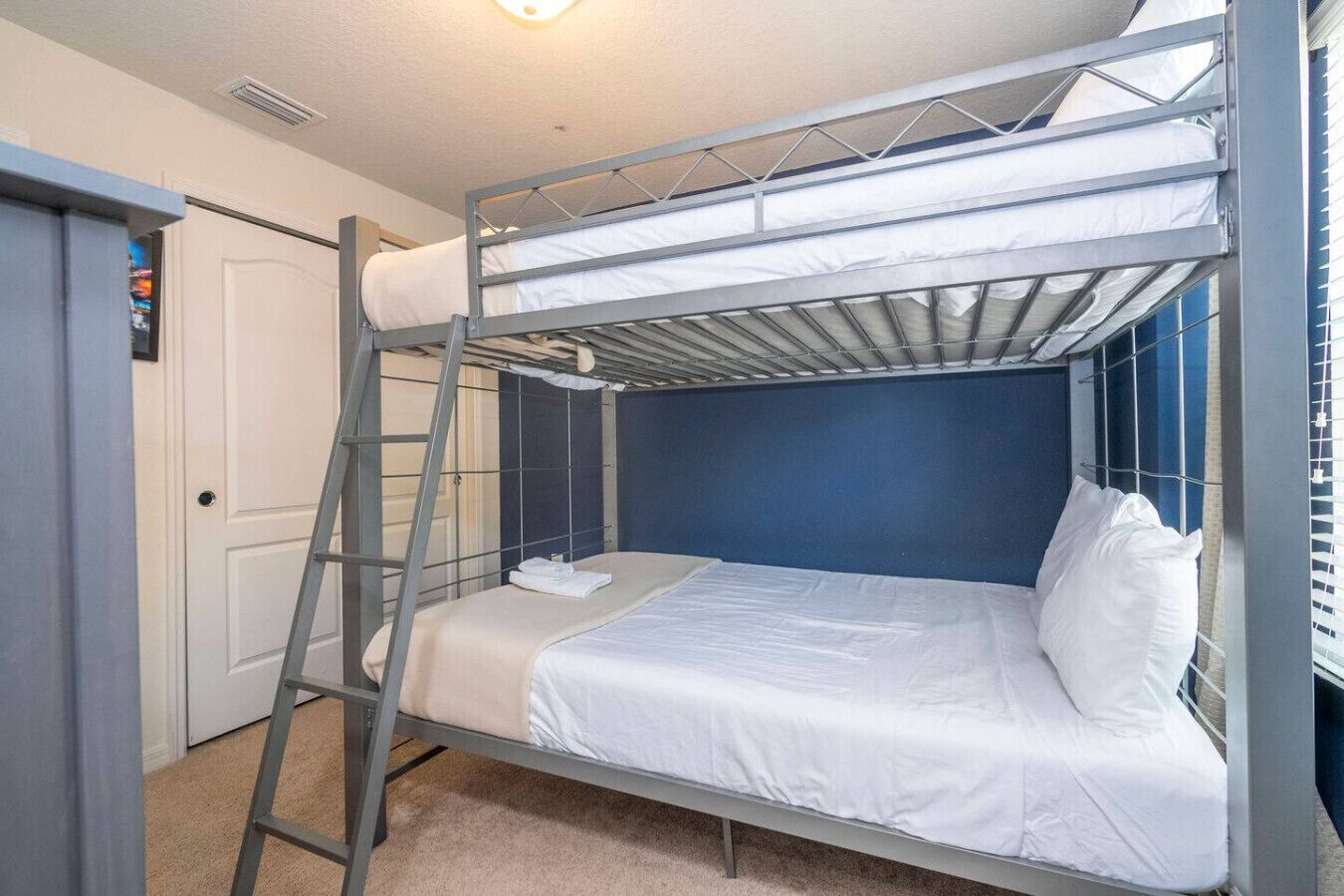 Quarto com beliche, escada, roupa de cama branca e parede azul.