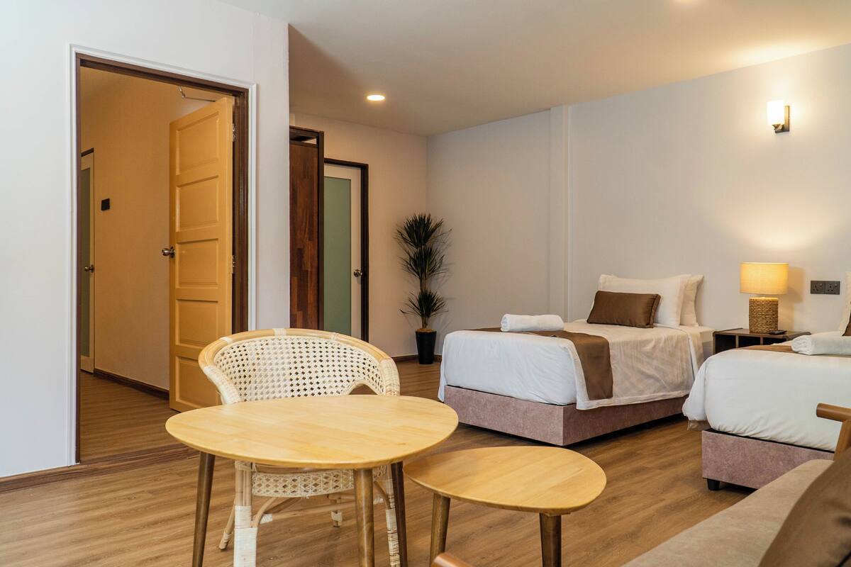 A hotel room with two beds, a small table, a chair, and a potted plant.