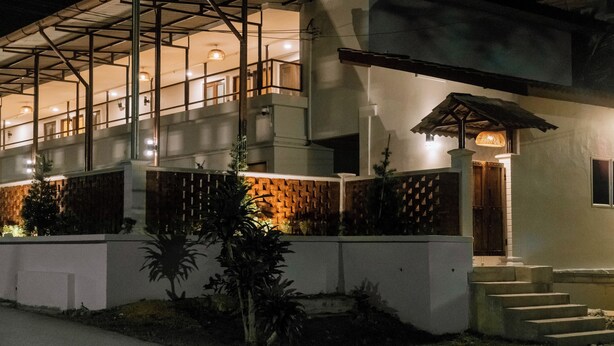 A multi-story building with a balcony on the upper floor, a wooden door, and a small porch with a lamp. - Mulyo Hotel (Port Dickson)