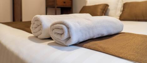 Una cama bien hecha con una toalla blanca enrollada, un plaid marrón y dos almohadas marrones.