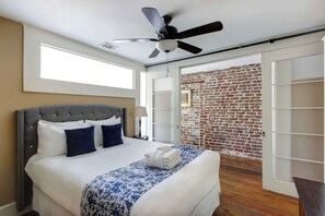 A hotel room with a bed, a ceiling fan, a brick wall, and a sliding door leading to a balcony. - The Factor’s Flat, Historic | River View (Savannah)