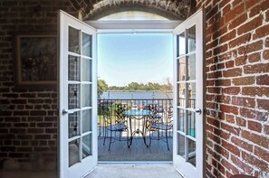 An open door leading to a balcony with a view of a body of water and parked cars. - The Factor’s Flat, Historic | River View (Savannah)