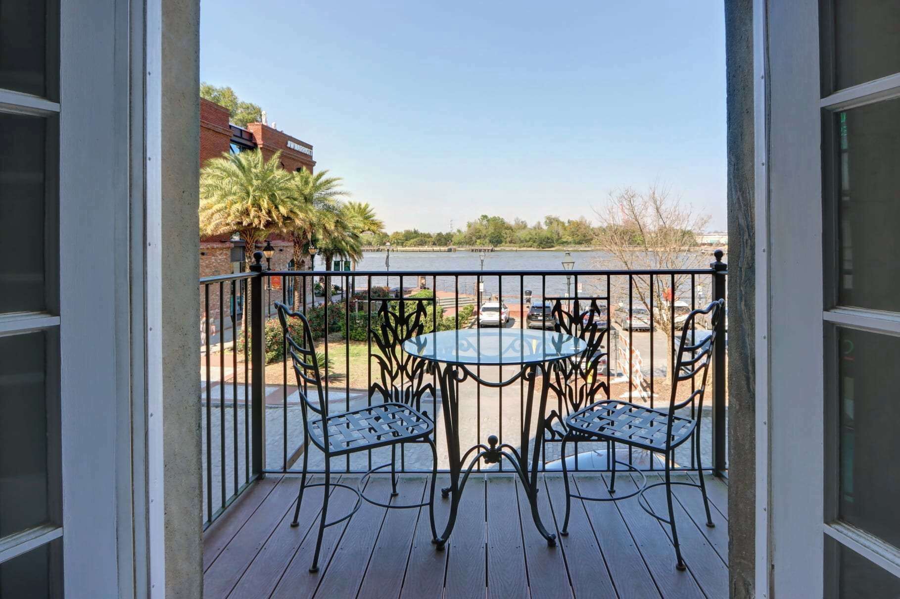 A balcony with a table and chairs, overlooking a parking area and a body of water.