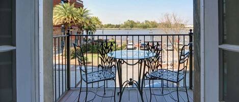 A balcony with a table and chairs, overlooking a parking area and a body of water.