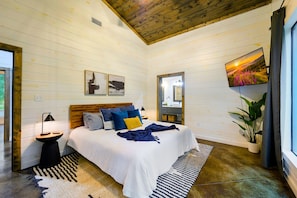 Un dormitorio con cama, mesita de noche, televisor y ventana.