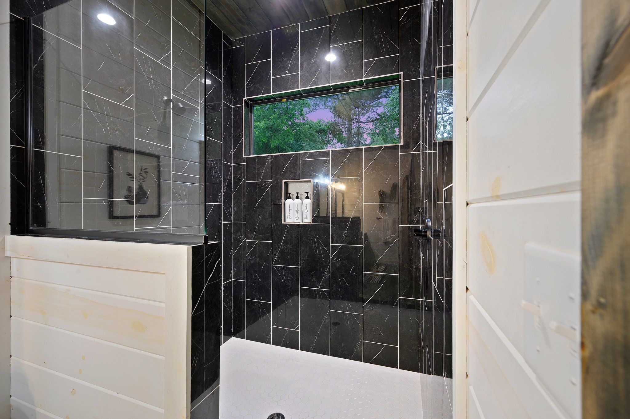 A bathroom with black marble tiles, a white sink, and a TV mounted on the wall.