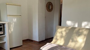 A living room with a sofa, a small white table, a woven rug, and a kitchen area with a white refrigerator. - Charmant Cabanon Provençal (Montfort-sur-Argens)