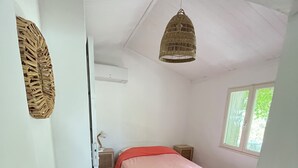 A bedroom with a bed, a nightstand, a wall-mounted air conditioner, and a window with a view of greenery. - Charmant Cabanon Provençal (Montfort-sur-Argens)