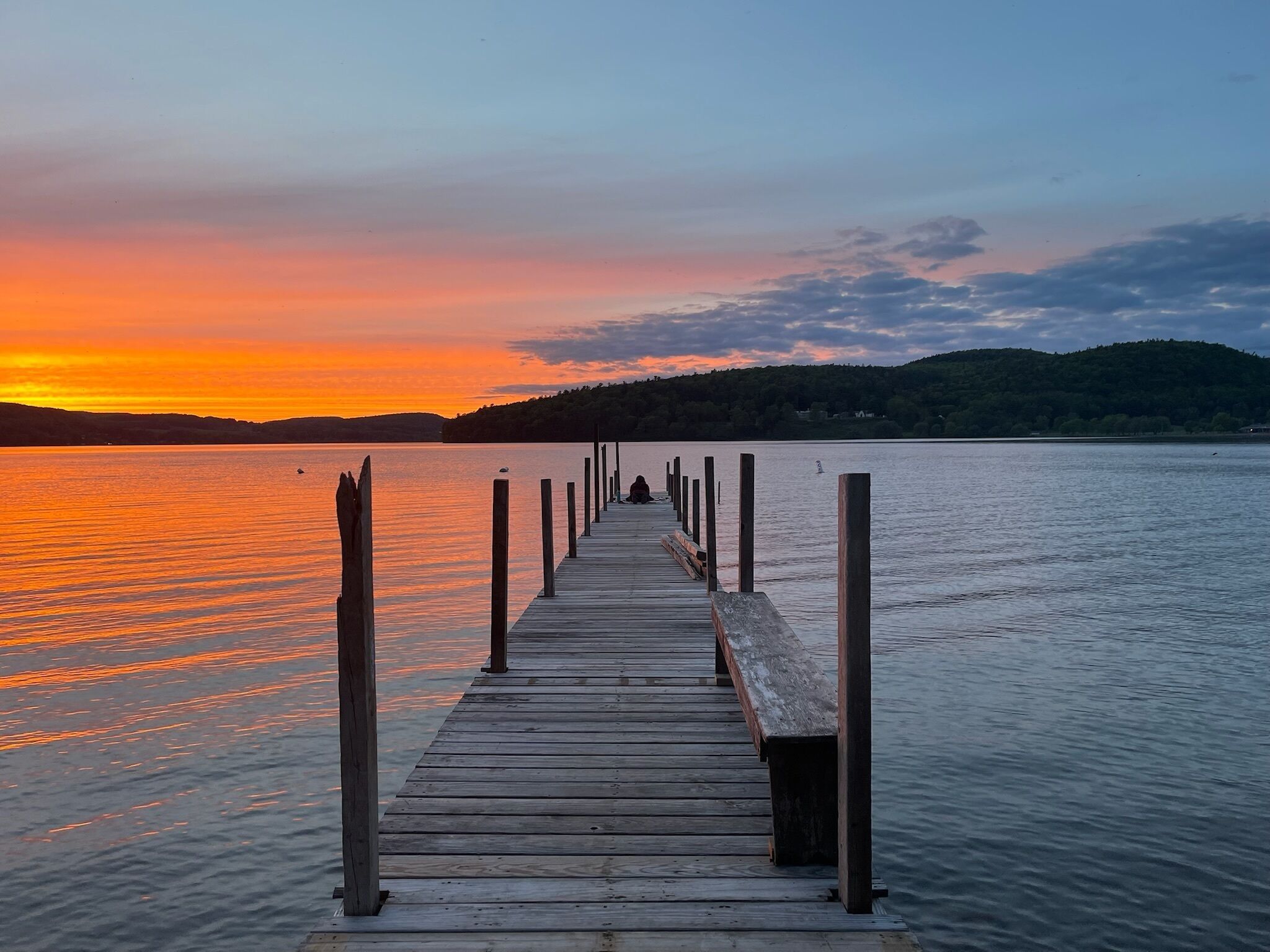 A wooden pier extending into calm water with a sunset in the background.