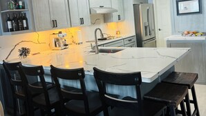 A modern kitchen with a central island, dark wooden chairs, and built-in appliances. - Panoramic Ocean Front view 3 bedroom 3 bath condo
STR License 2024-0443 (South Padre Island)