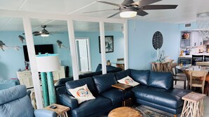 A modern living room with a blue leather sofa, a wooden coffee table, and a unique wooden stool. - Panoramic Ocean Front view 3 bedroom 3 bath condo
STR License 2024-0443 (South Padre Island)