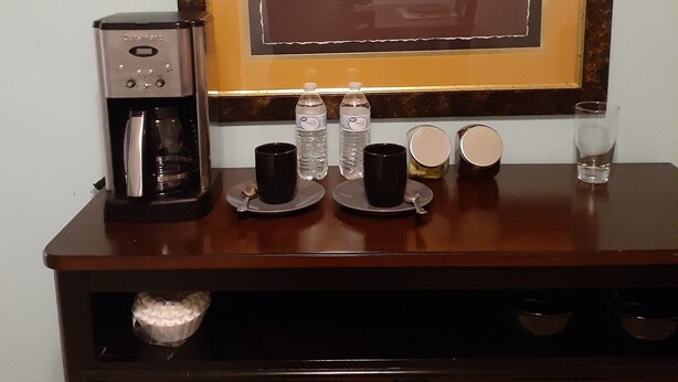 Une machine à café, deux tasses, deux bouteilles d’eau, un verre et un tableau encadré représentant un tigre, le tout posé sur un comptoir en bois.
