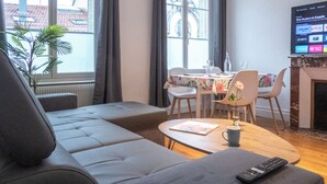A modern living room with a grey sofa, a wooden coffee table, and a TV mounted on the wall displaying a streaming service interface. - Paradis - Cosy Comfy 3Beds 70m² Central FastWiFi SmartTV55" PrimeVideo BBQ (Verdun)