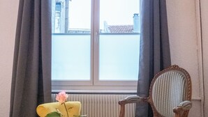 A room with a window, a yellow chair, a wooden chair, a small table, and a rose in a glass. - Paradis - Cosy Comfy 3Beds 70m² Central FastWiFi SmartTV55" PrimeVideo BBQ (Verdun)
